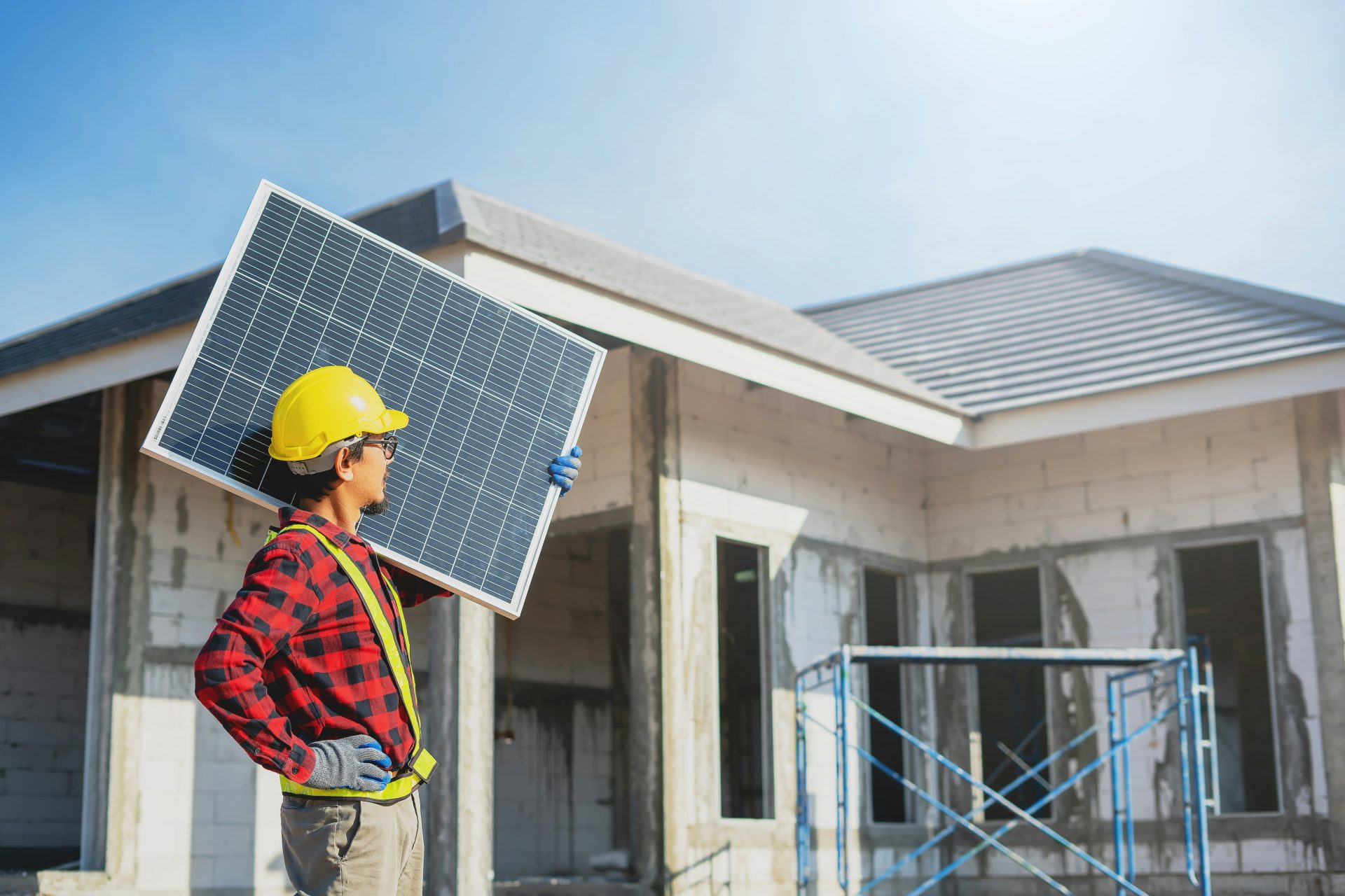A man holding a solar panel in front of a house